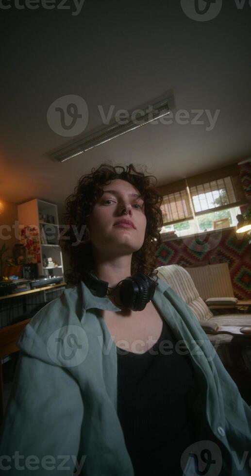 A young woman smiles looking at the camera as if she is taking selfie on a mobile phone. She's sitting on the bed at home photo