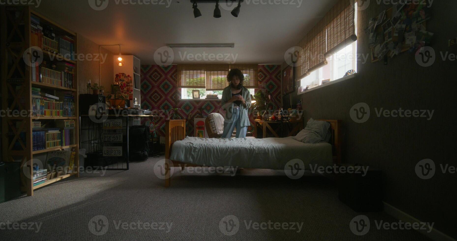 A young woman uses a mobile phone at home. She walks around the bedroom with a serious look. photo