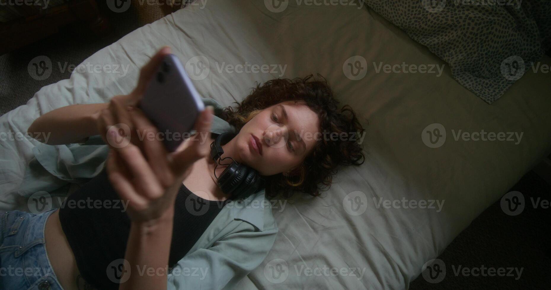 A young woman sends a message on her mobile phone and feel depressed lying on the bed photo