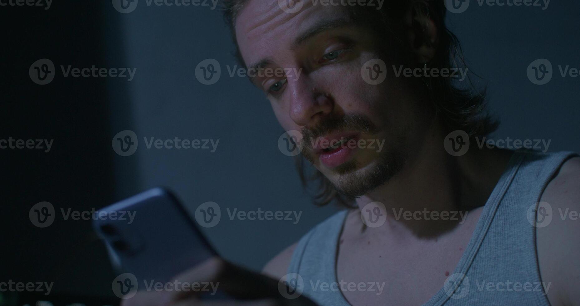 A man uses a mobile phone while sitting at home at night. He wipes away his tears photo