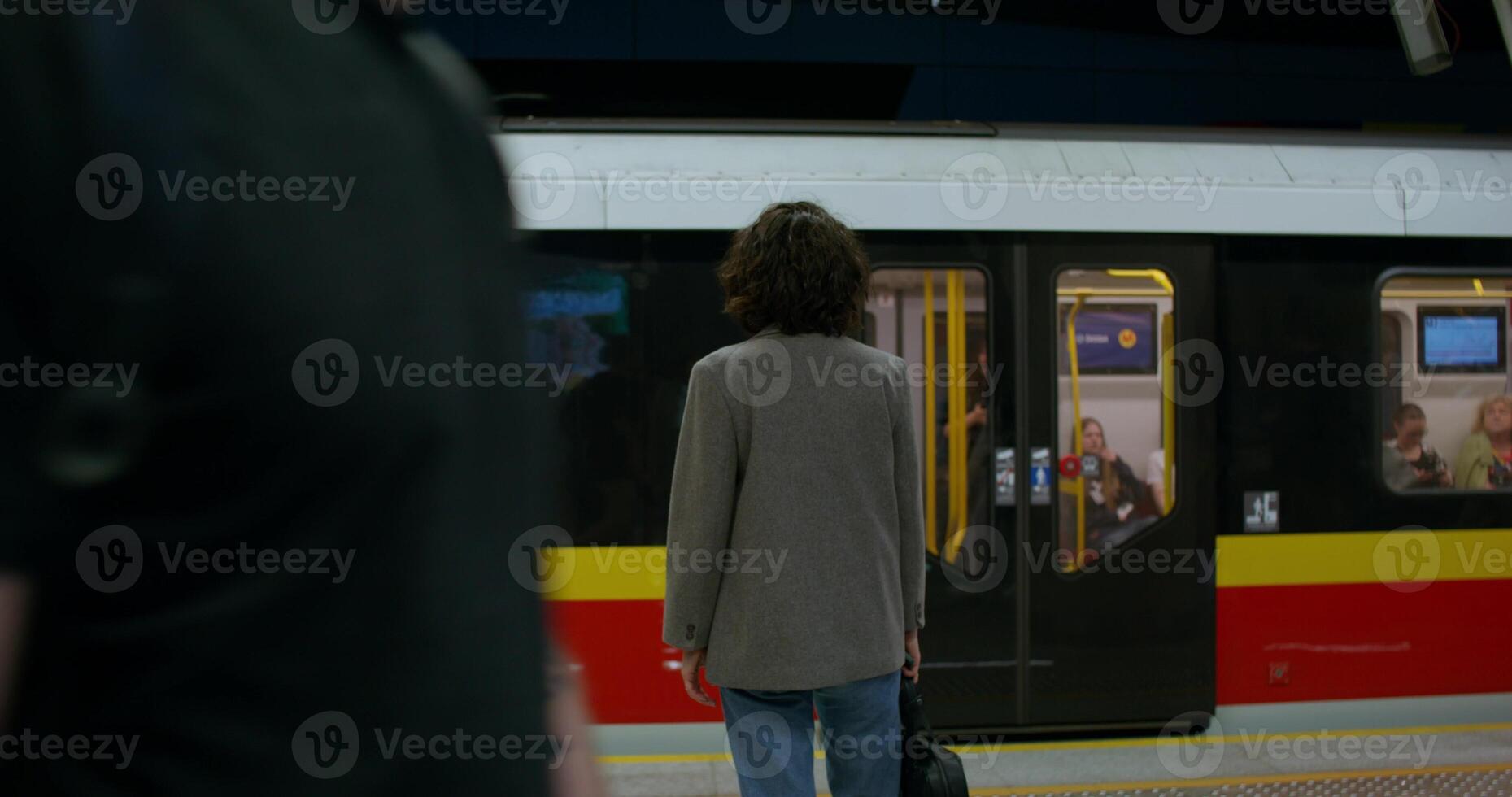 A stylish woman stands on a subway platform. The train is going past her. Rear view, unrecognizable person photo