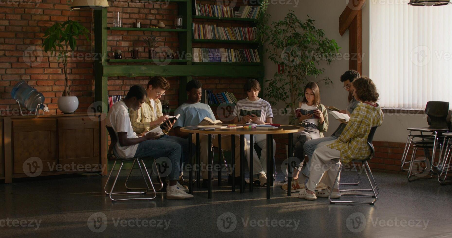 Group of young people of different nationalities are reading the Bible together while sitting at a table indoors. A woman reads aloud photo
