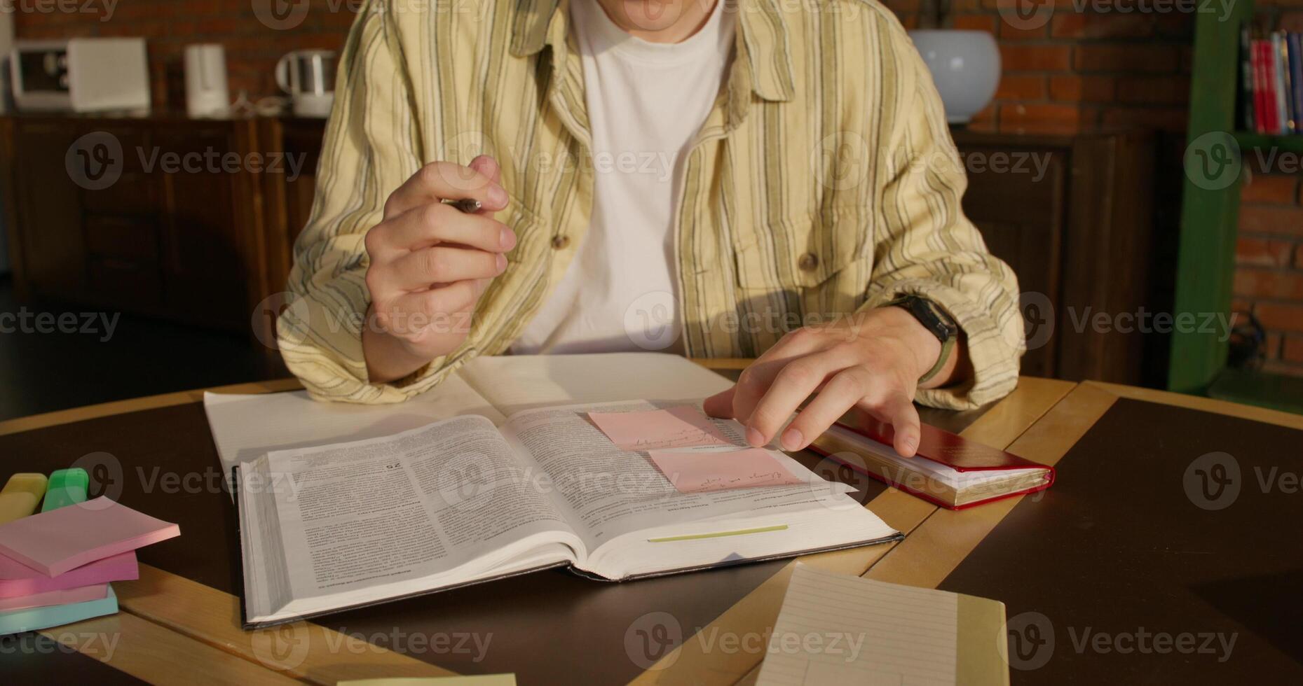 A man is studying the Bible while sitting at a table indoors. He writes notes on stickers. Daylight photo