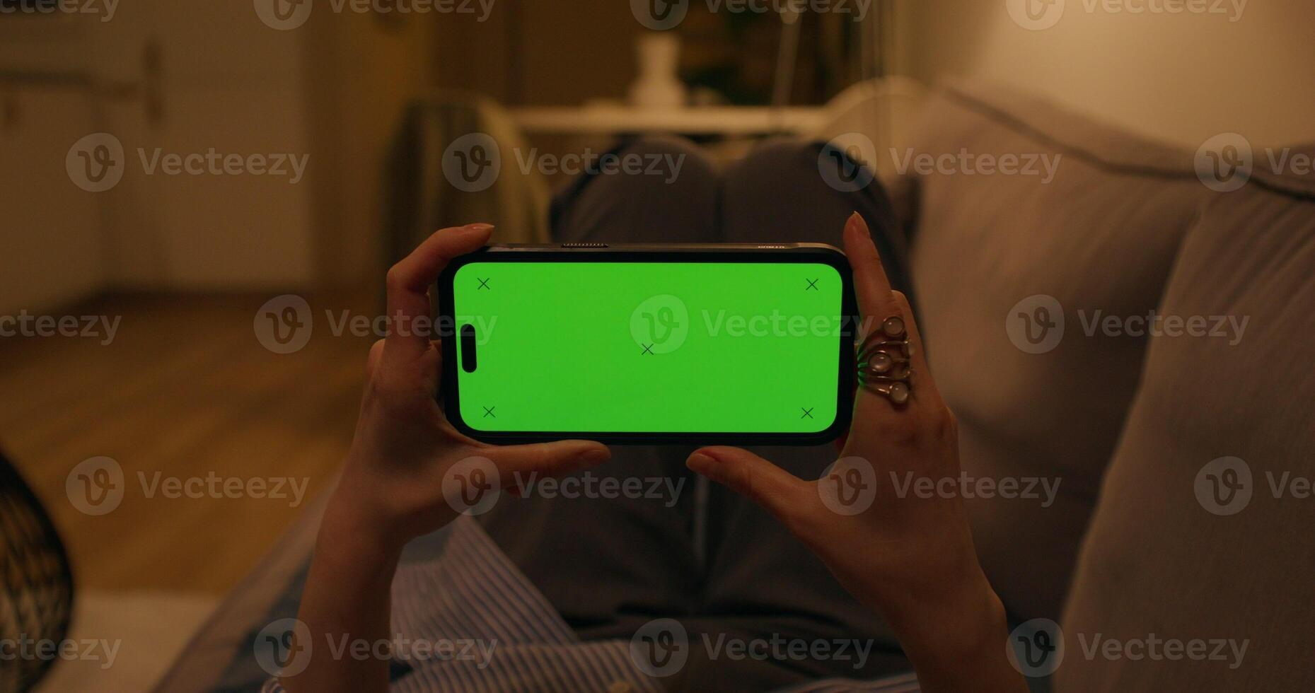 A woman uses a mobile phone with a green screen lying on the couch at home, close-up of her hands, an unrecognizable person, dimmed evening light photo