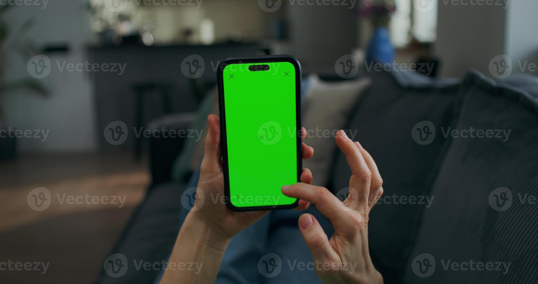 A woman uses a mobile phone with green screen lying on the couch at home, close-up of her hands, an unrecognizable person photo