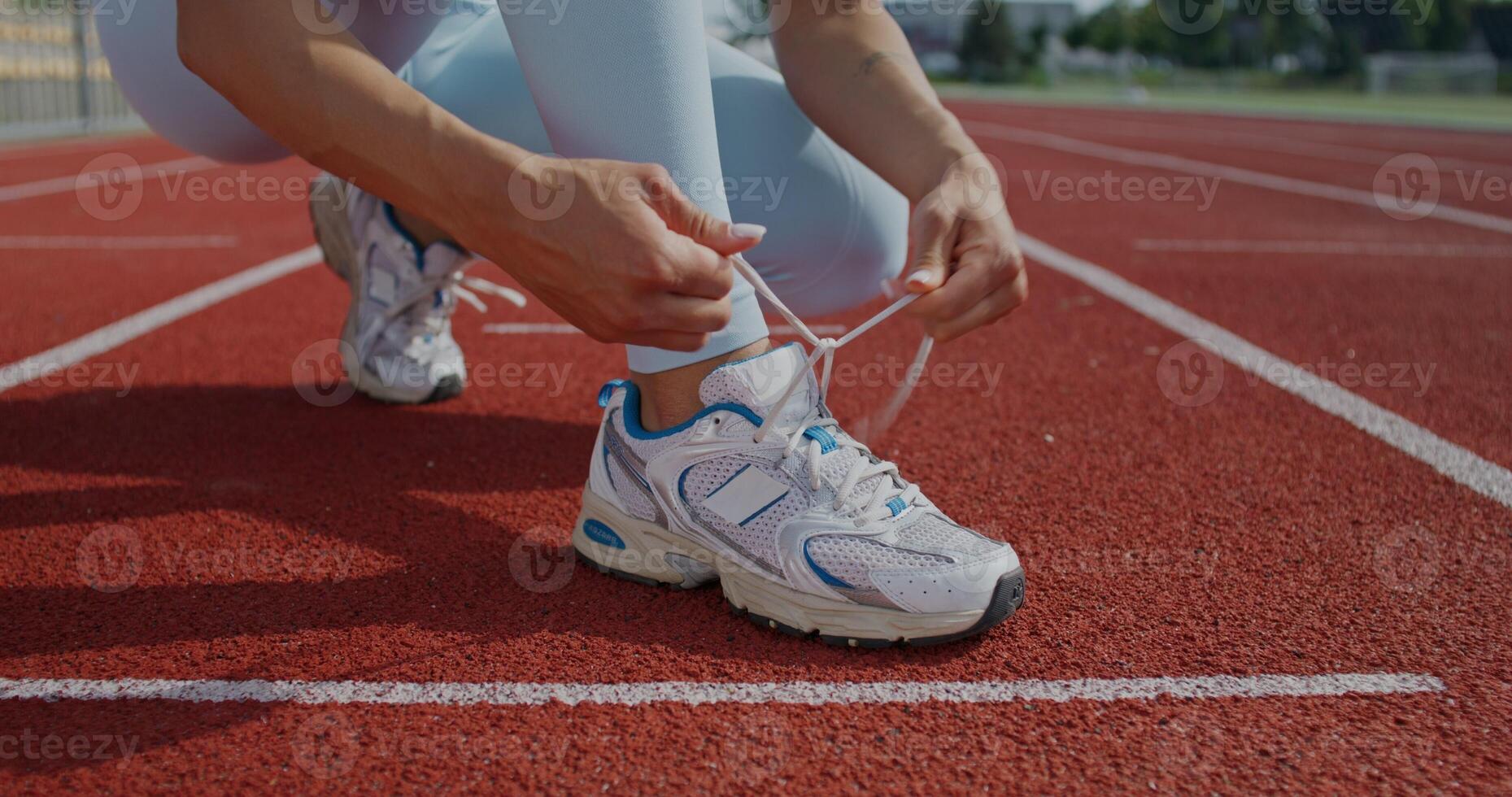 A woman in sportswear ties her shoelaces on sneakers standing at the stadium. Close-up of her hands, an unrecognizable person. She is getting ready for a run on a summer day photo