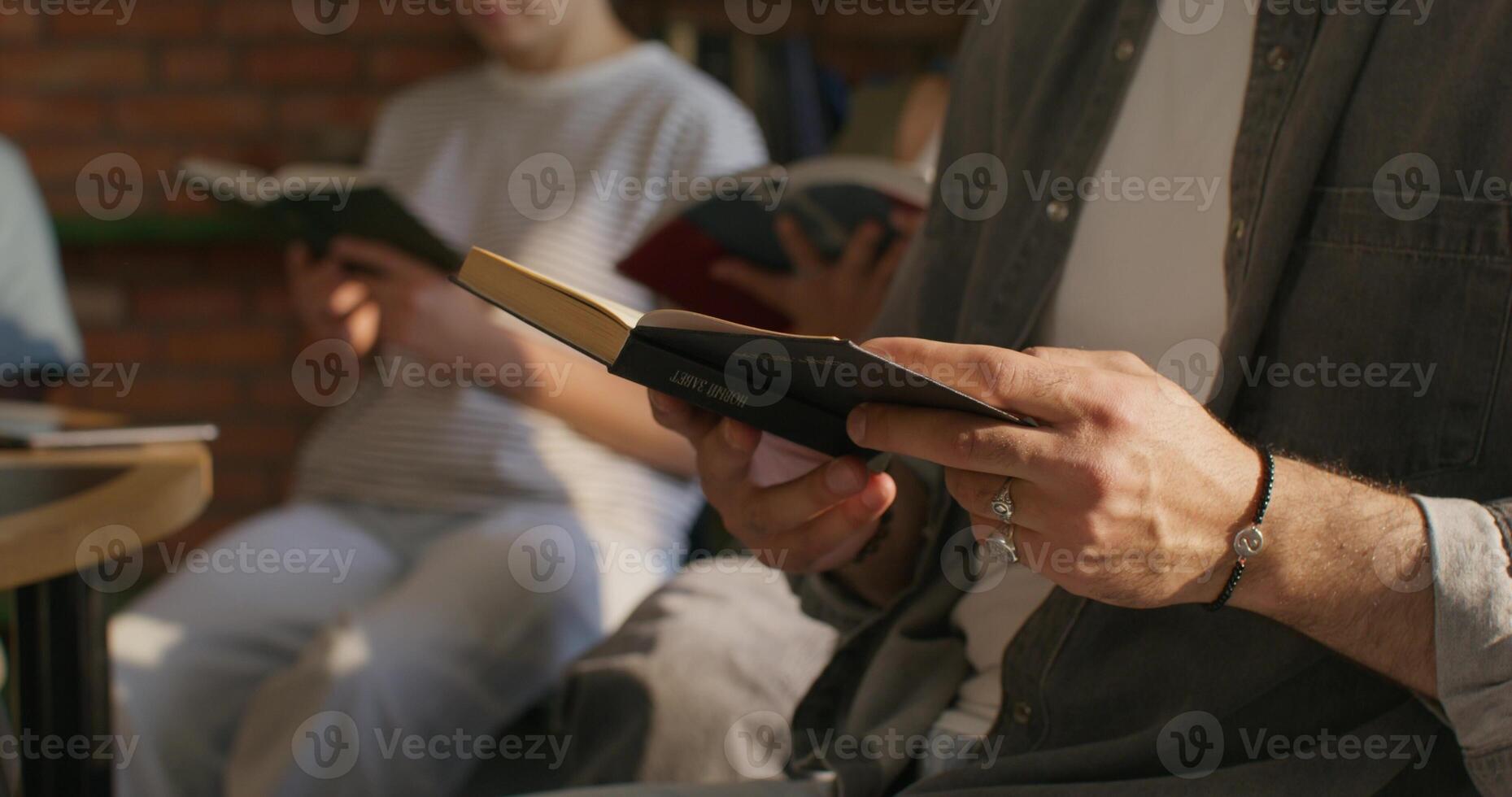A man and a woman hold Bibles in their hands, sitting at a table indoors, close-up of their hands, unrecognizable persons. Daylight photo