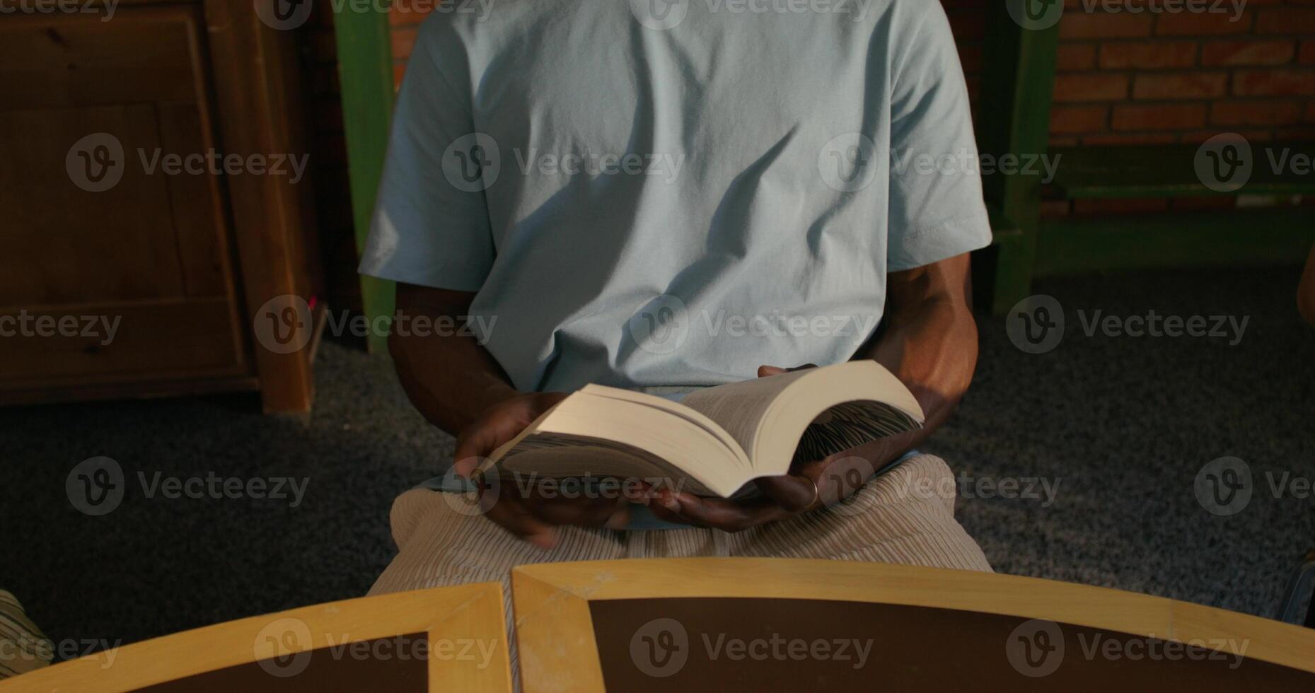 A man is flipping through the Bible while sitting indoors. The moves from his hands to his face. Daylight photo