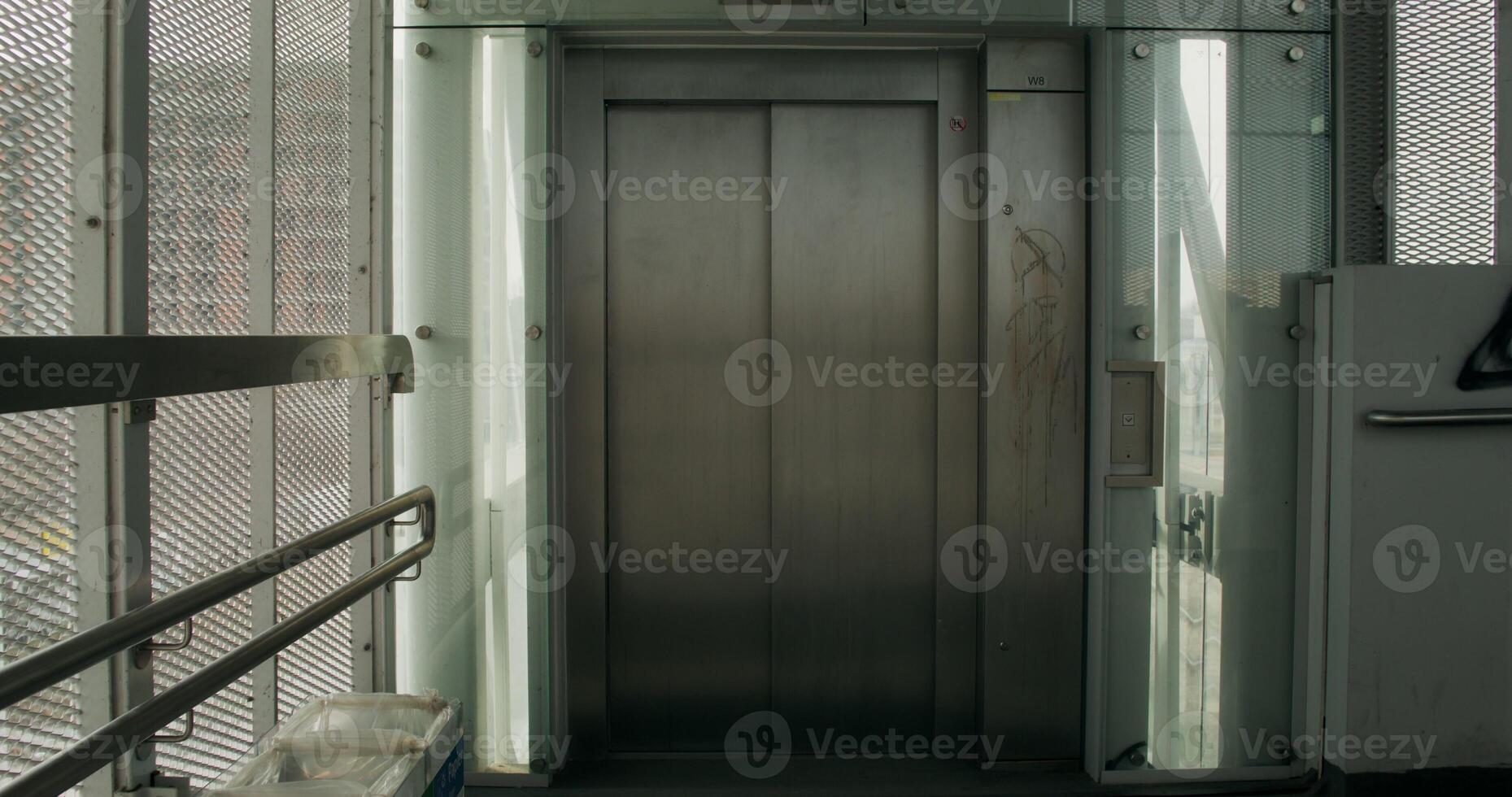 A woman in formal clothes and a coat uses a mobile phone coming out of the elevator. She's rolling a suitcase photo