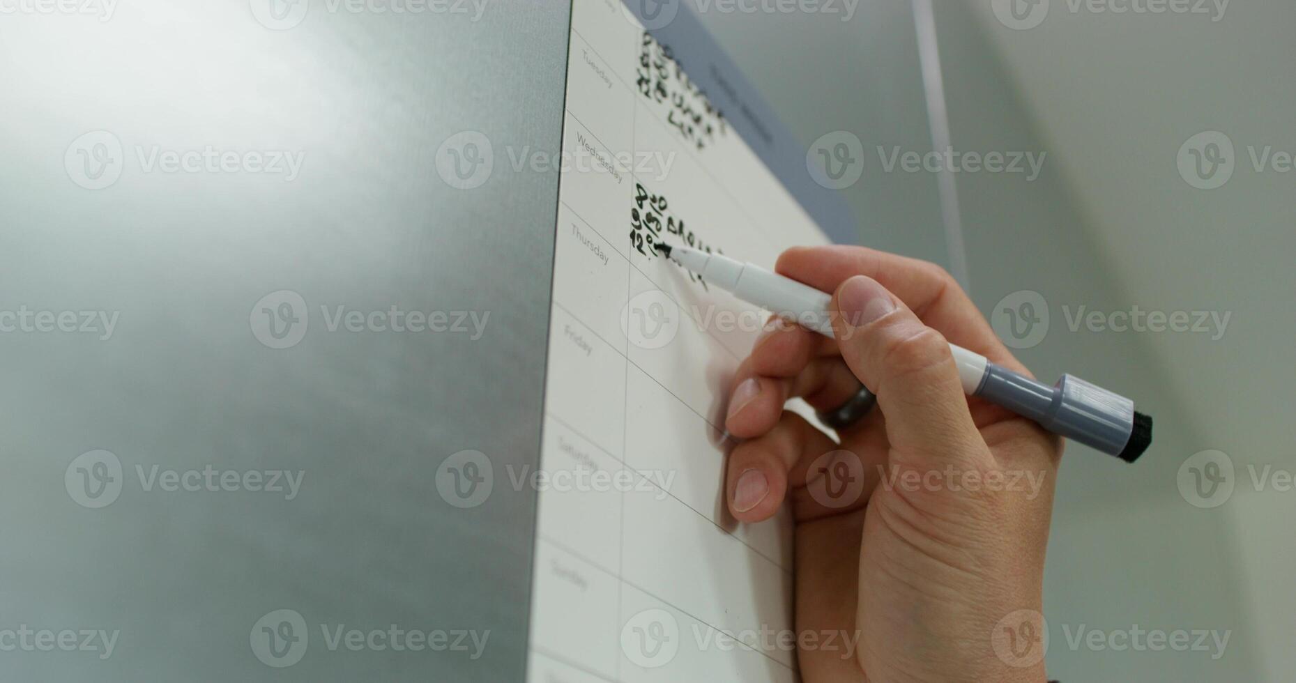 A man in casual clothes fills out a chart with a schedule hanging on the kitchen cabinet. close-up of his hand, an unrecognizable person photo