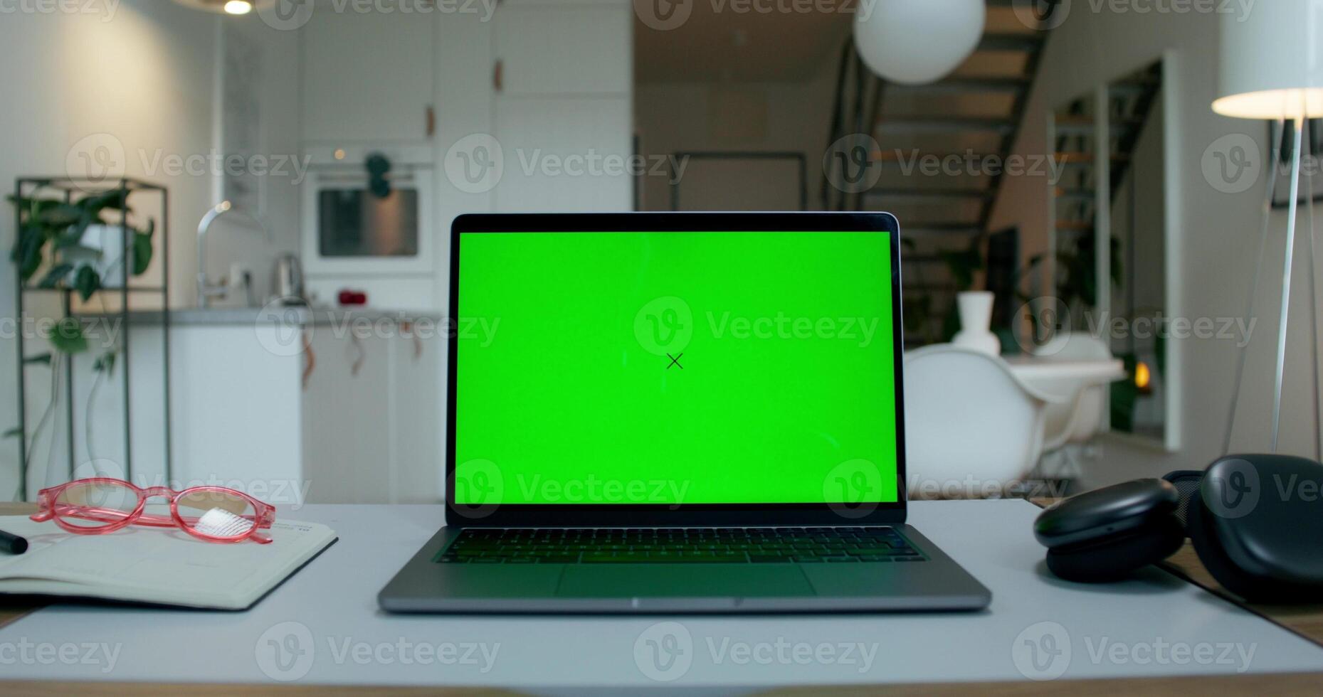 A laptop with a green screen is on the desktop at home. An open notebook and headphones next to it. A man's hand presses a laptop key photo