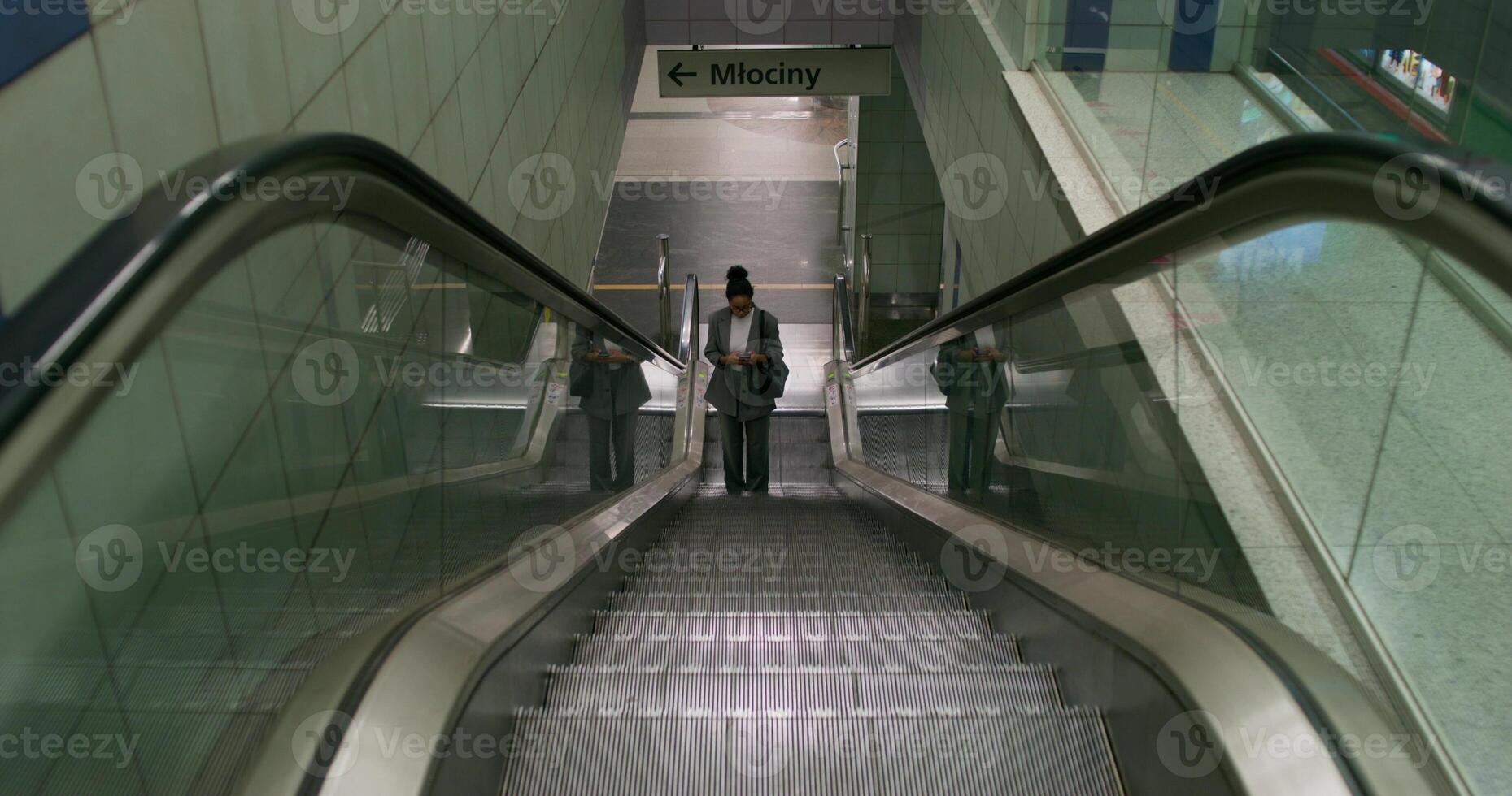 A woman in formal clothes rides an escalator up, she goes up from the subway station. She holds a mobile phone in her hand photo