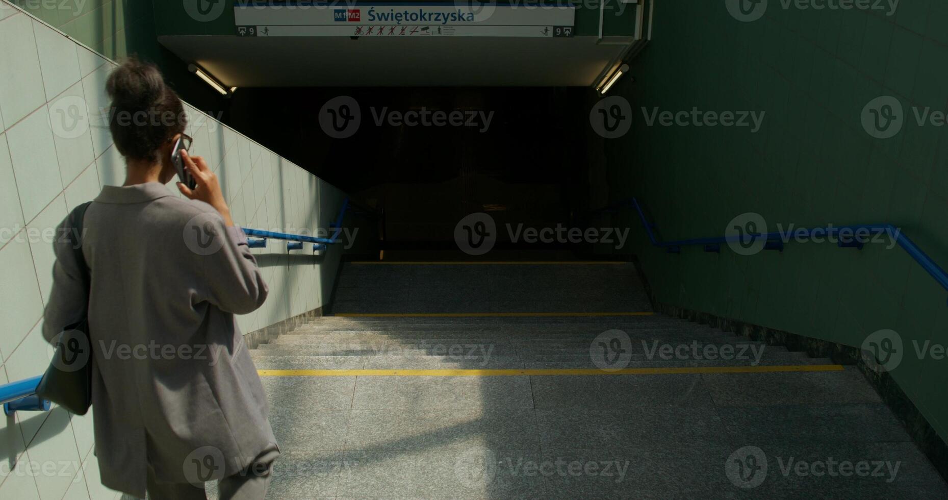 A woman in formal clothes is talking on a mobile phone going down the stairs to the subway station. Rear view, unrecognizable person photo