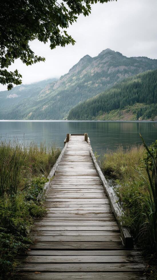 Tranquil Wooden Dock Extends Over Calm Lake Surrounded by Mountains on a Cloudy Day. photo