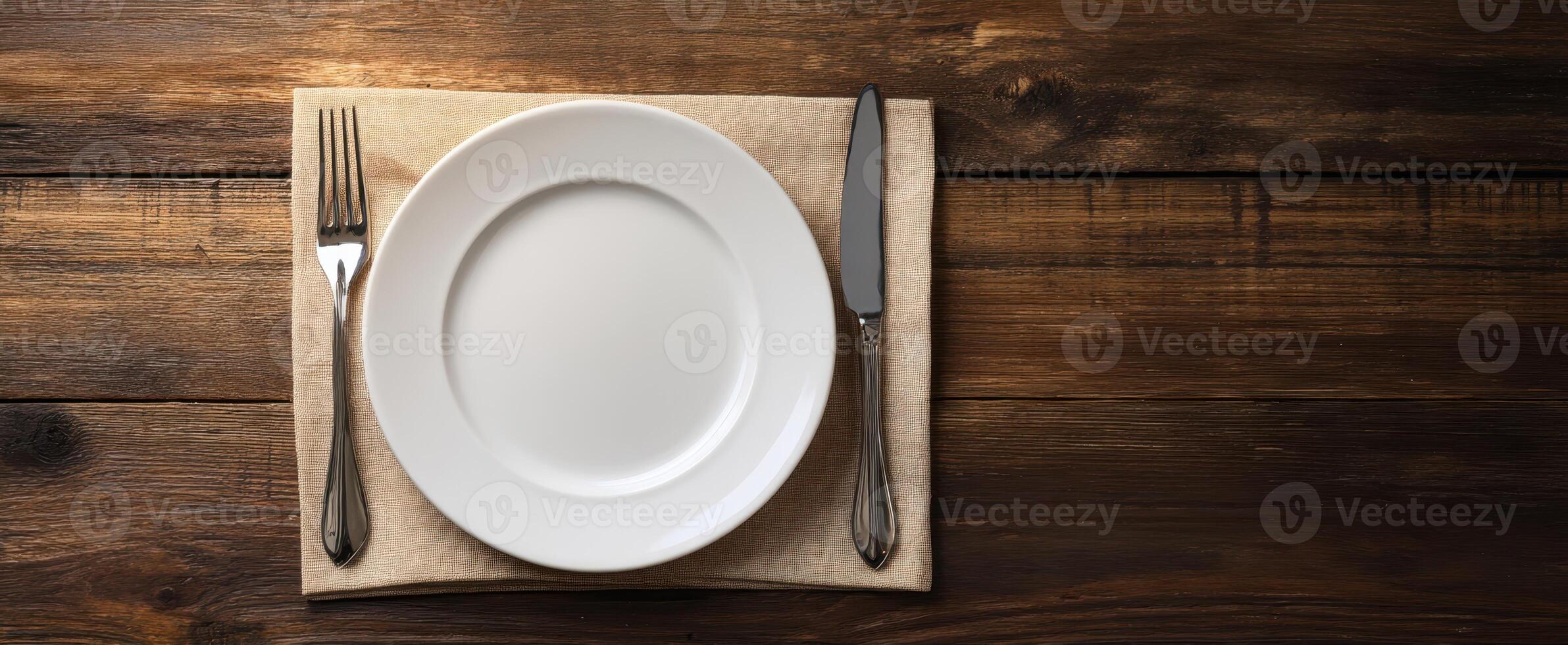 The elegant dining setting with a white plate and cutlery on a wooden table. photo