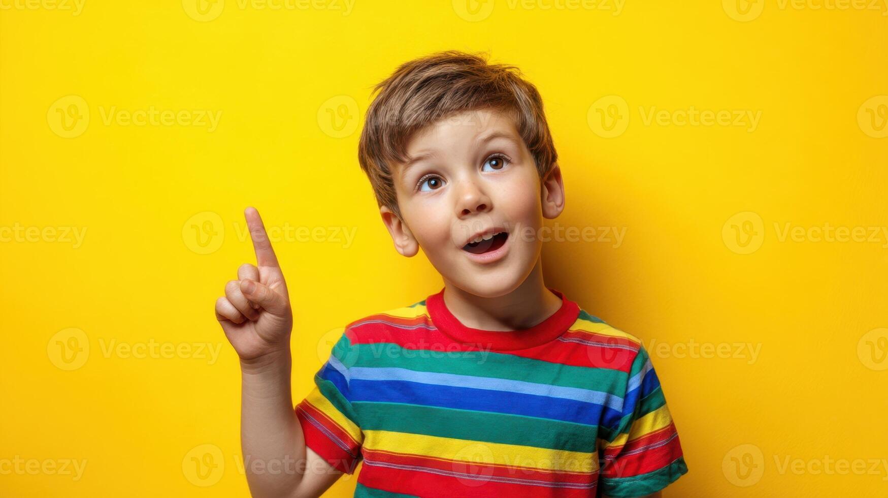 The cheerful boy with a colorful shirt pointing to an idea against a yellow background. photo