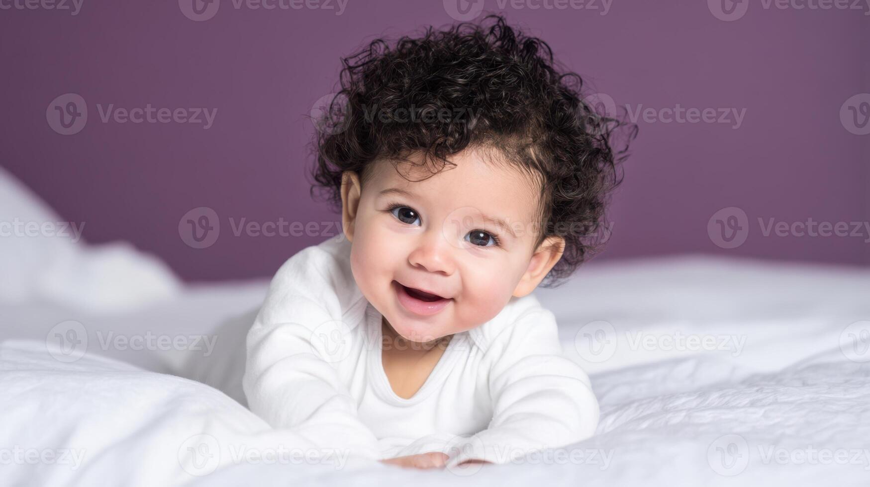 The adorable baby with curly hair smiling on a cozy white bed. photo