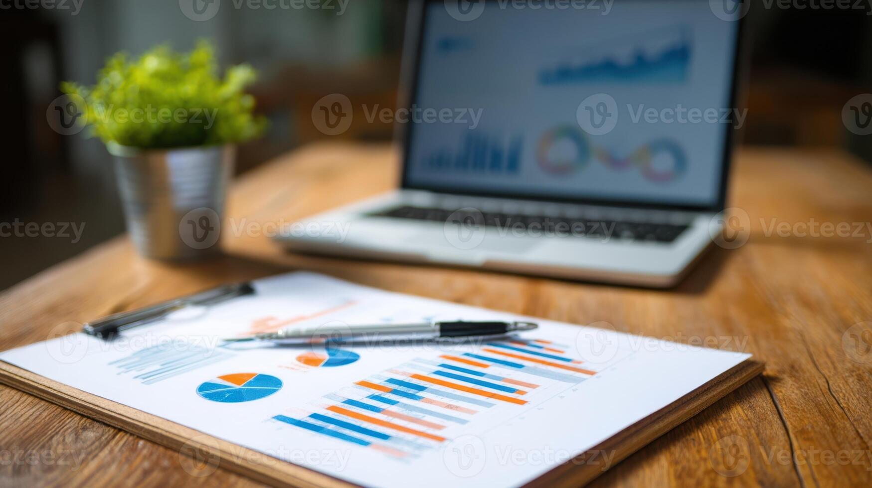 The document with charts and graphs on a wooden desk beside a laptop. photo