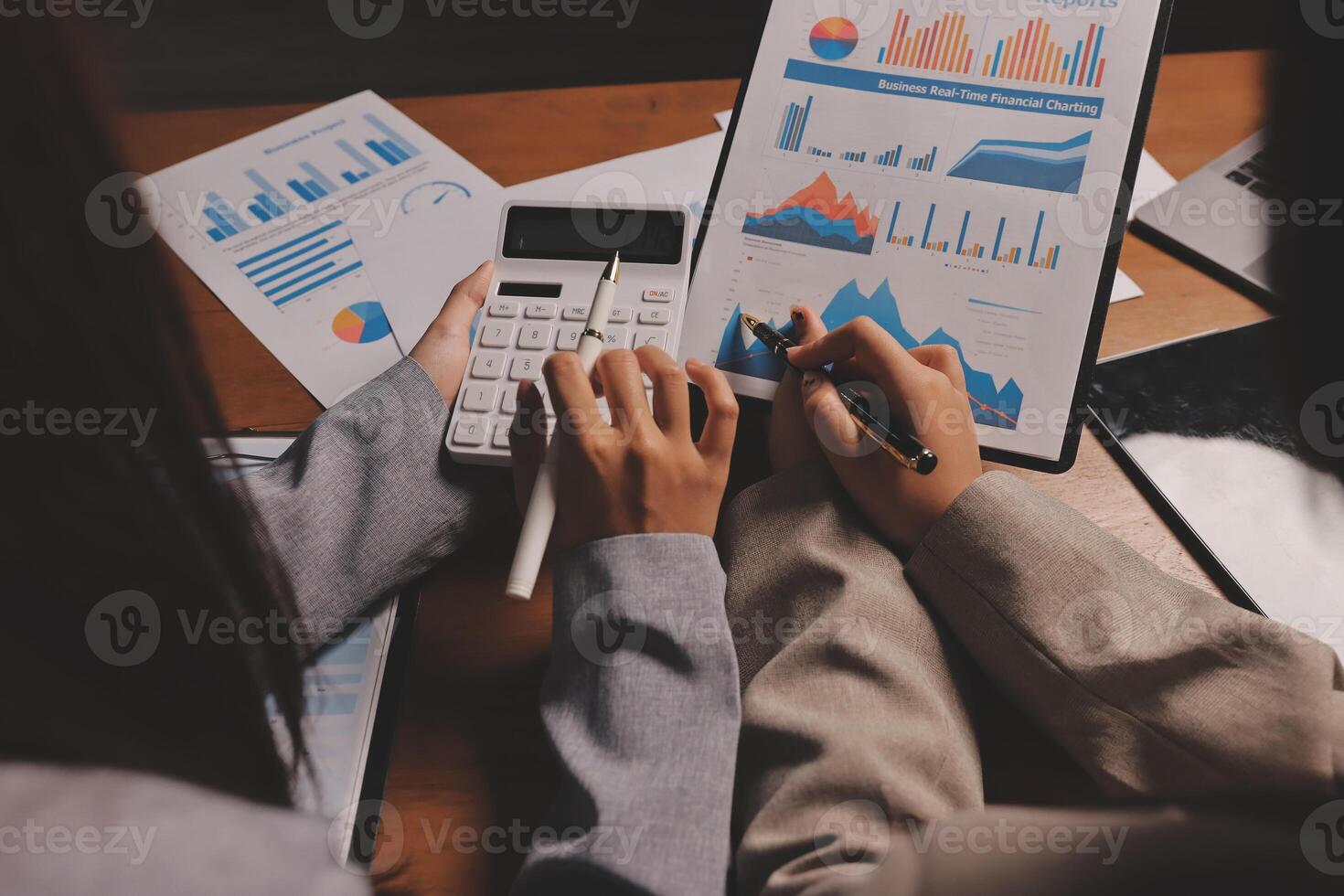 Two business people are working on a calculator and paper with graphs photo
