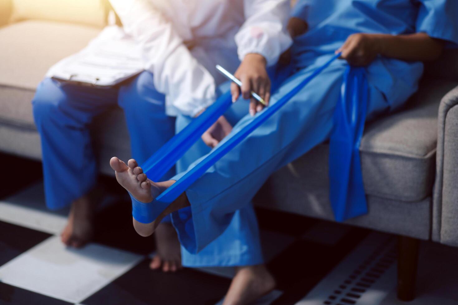 A woman in scrub clothes is sitting on a couch with a blue bandage on her foot photo