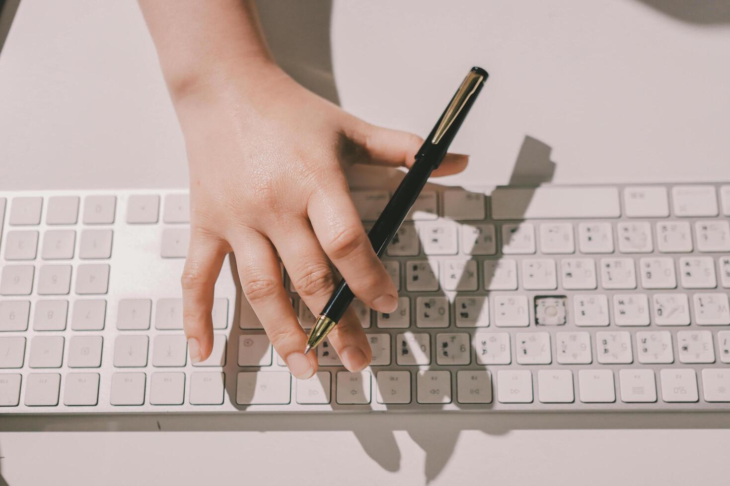 A person's hand on a keyboard with a pen photo