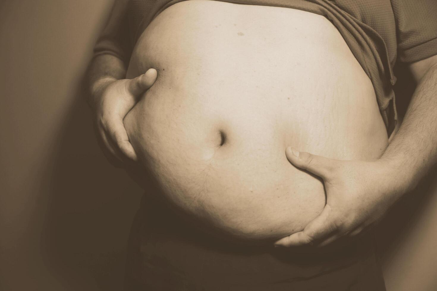 A man with a big belly holding his hands to his belly photo