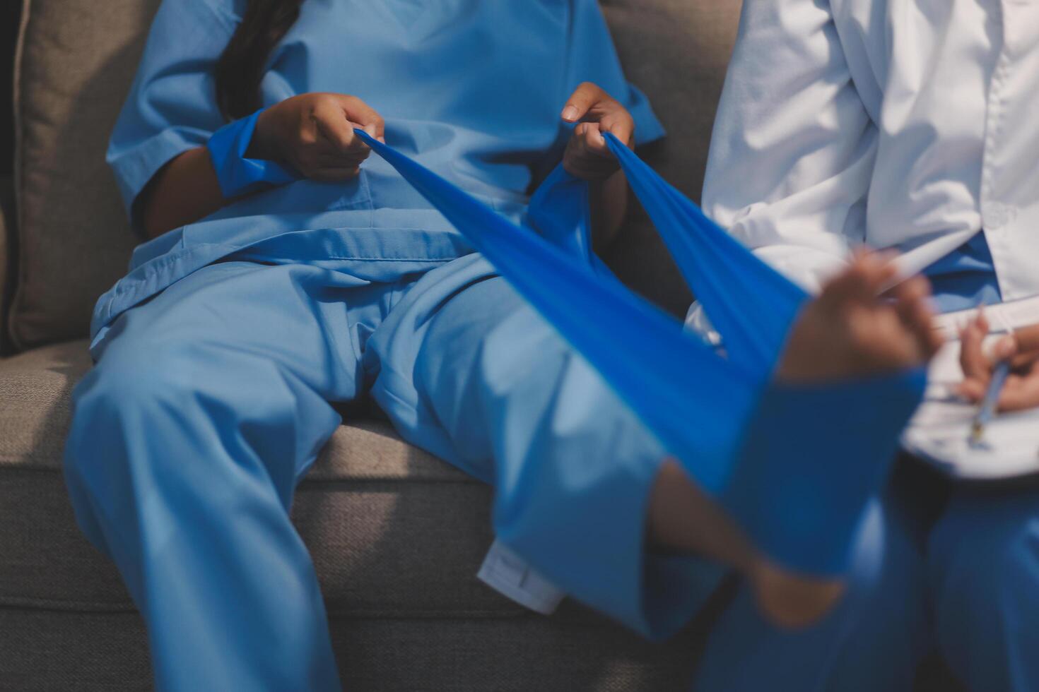 A woman in scrubs sitting on a couch with a blue bandage on her foot photo