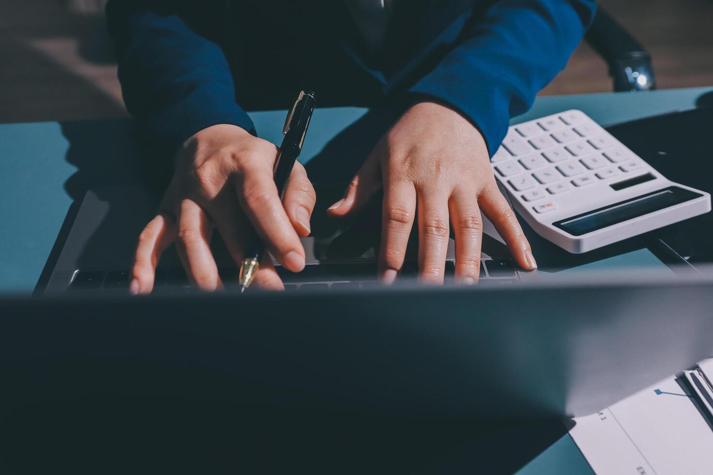 A person is typing on a laptop computer with a pen and calculator photo