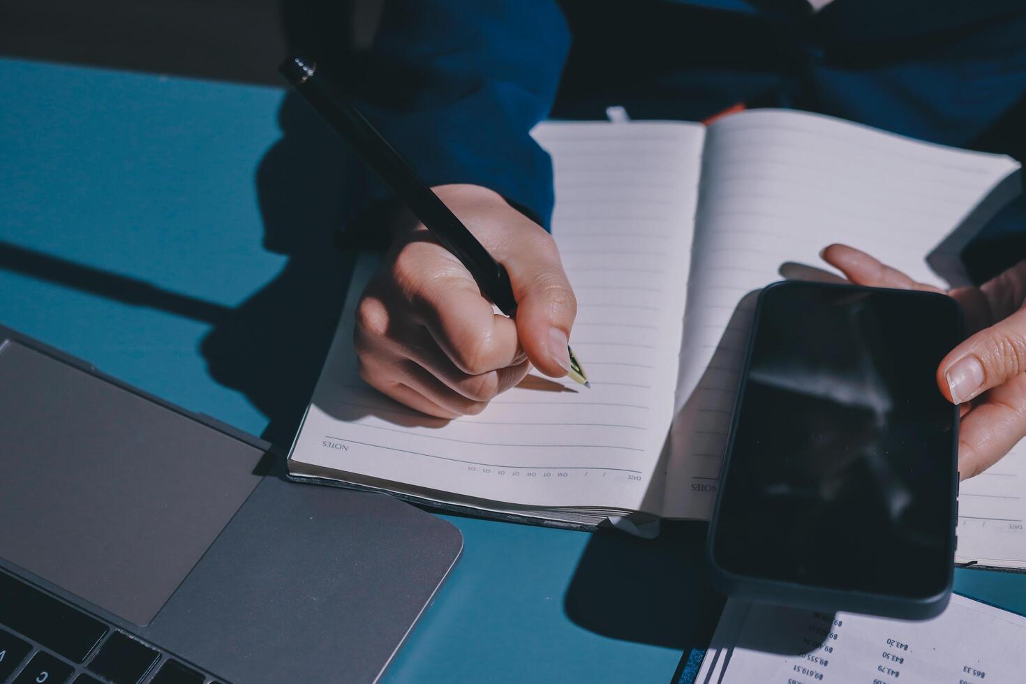 A person is writing on a notebook with a pen and a phone photo
