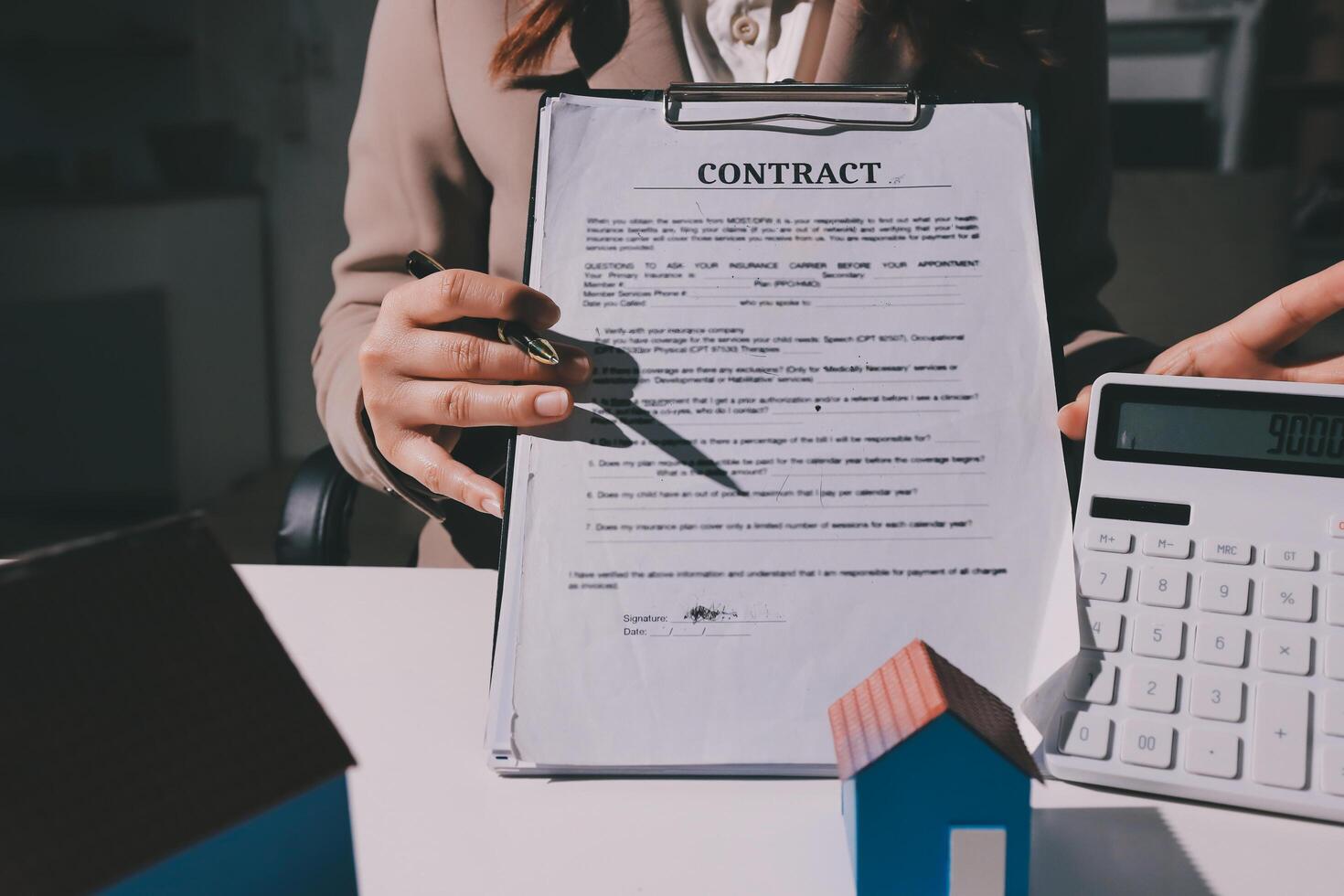A woman holding a contract and calculator in front of a house photo