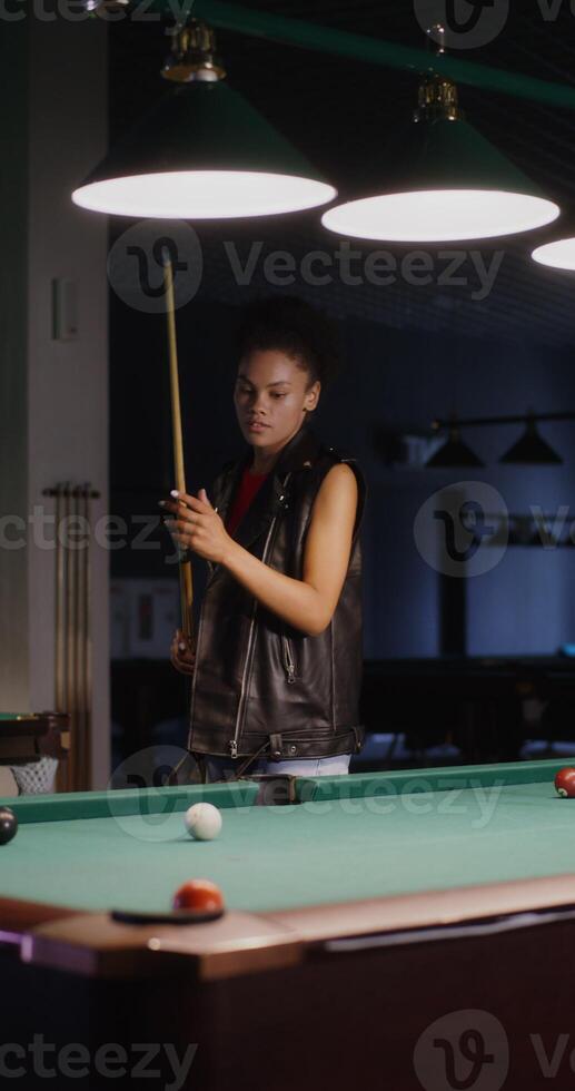 A young beautiful African-American girl is intently aiming a cue at the ball while playing billiards, but she fails to hit the hole, vertical - aiming photo