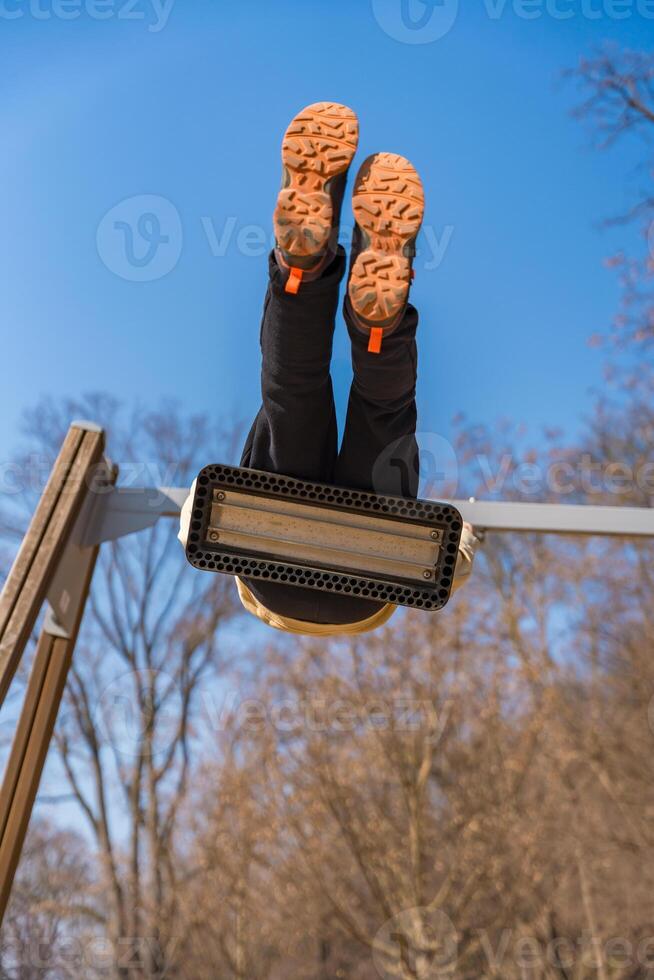 Child swinging upside down on swing seat in park, view from below, sunny winter day photo