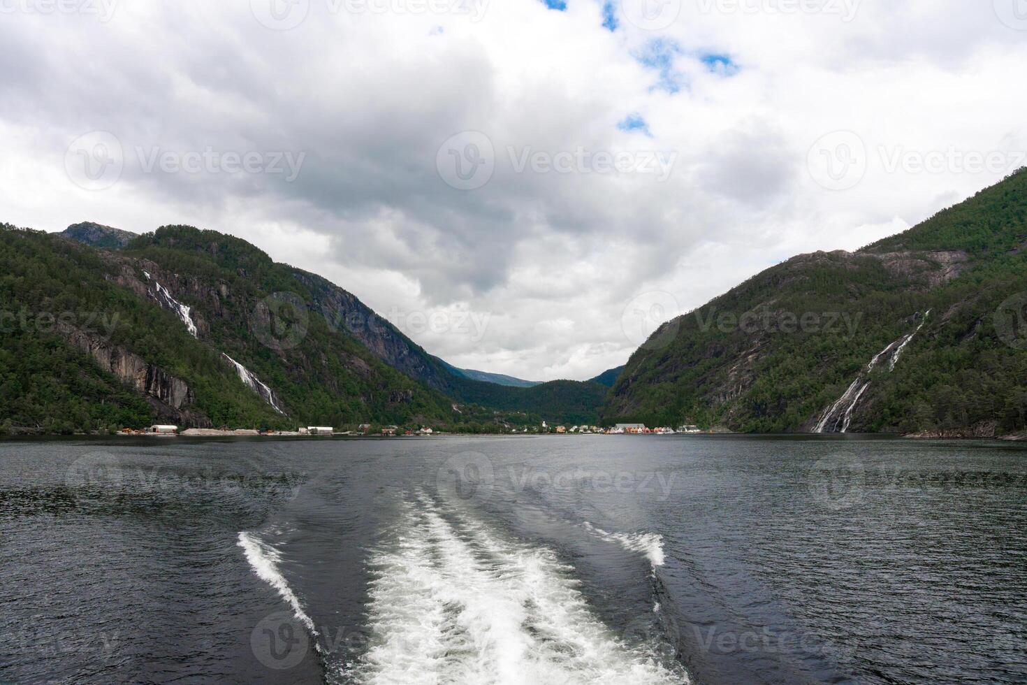 Fjord village and twin waterfalls seen from catamaran wake near Bergen, Norway photo