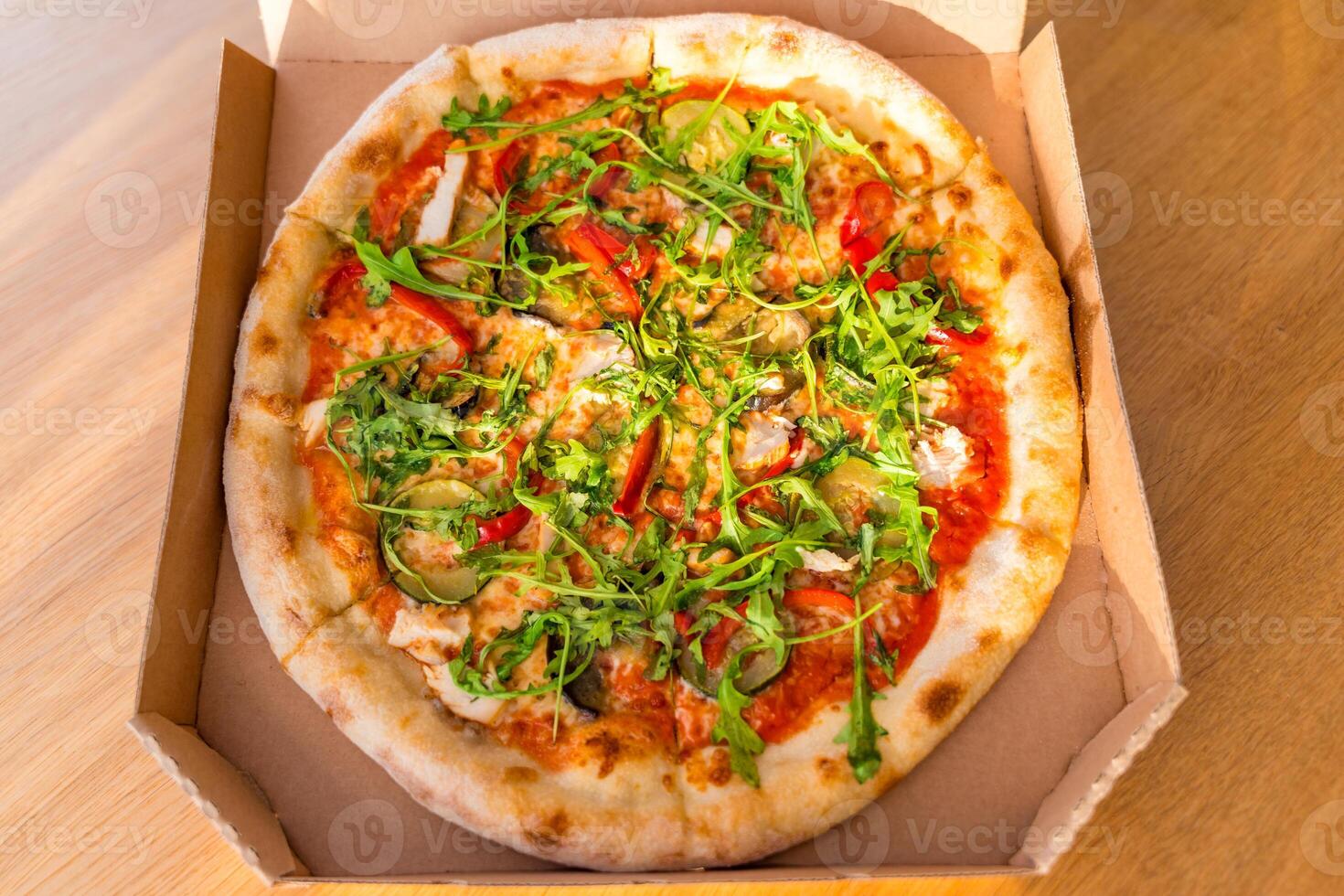 Fresh vegetable pizza with arugula in cardboard box on wooden table, sunlight, selective focus photo