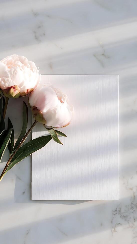 Elegant blank card with pale pink peonies on marble, bathed in soft light photo