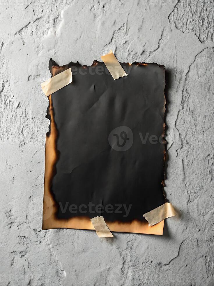 Burnt paper attached to a rough grey wall with adhesive tapes photo