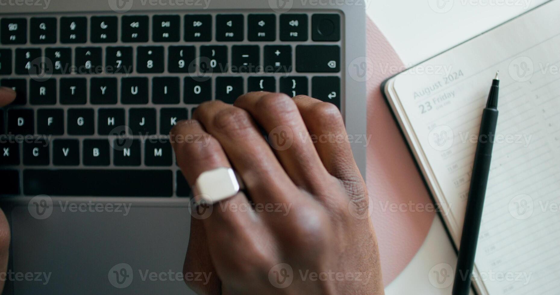 A man typing on a laptop, sitting at a table indoors, close-up of his hands, an unrecognizable person, view from above. An open notebook is on the table photo
