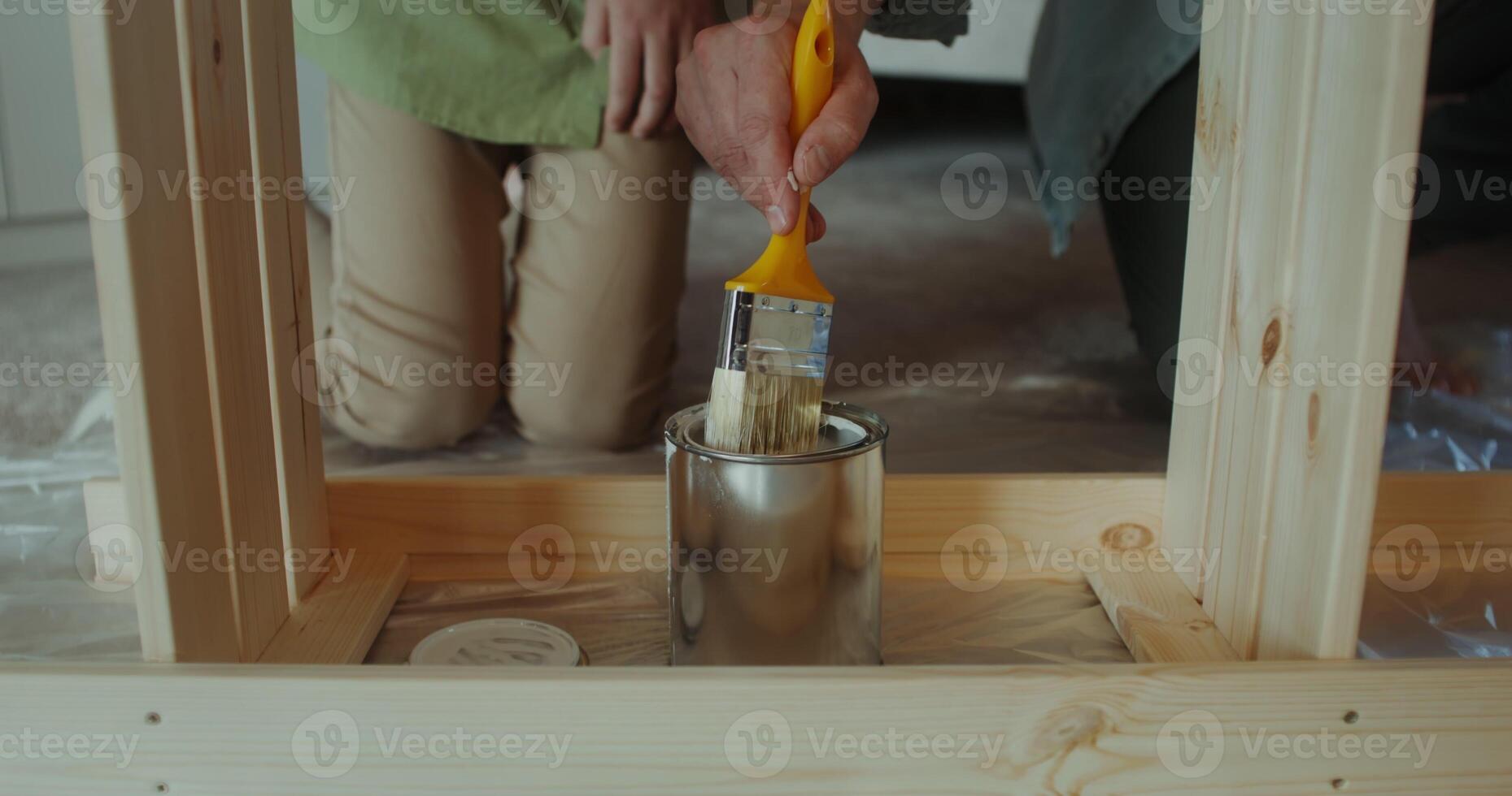 A father and son of European appearance paint a rack using brushes, sitting in a home interior, they smile and talk - father photo