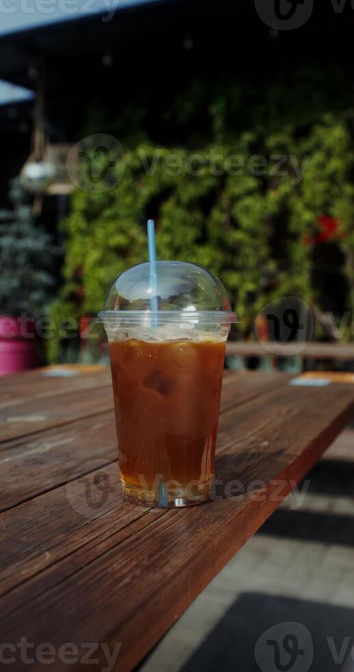 A disposable glass of lemonade is on the table, women's hands are stirring the drink with a straw photo