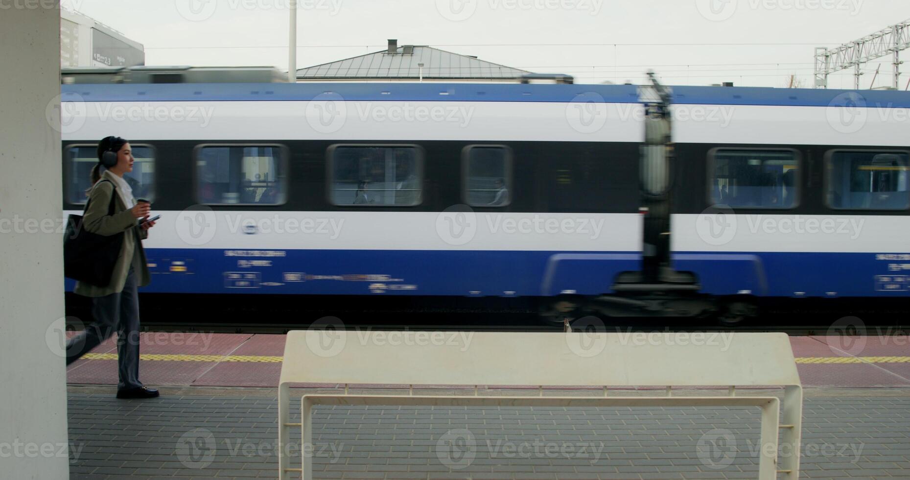 A woman in formal clothes and headphones, with a cup of coffee in her hand, descends the stairs to the platform of the railway station - coffee photo