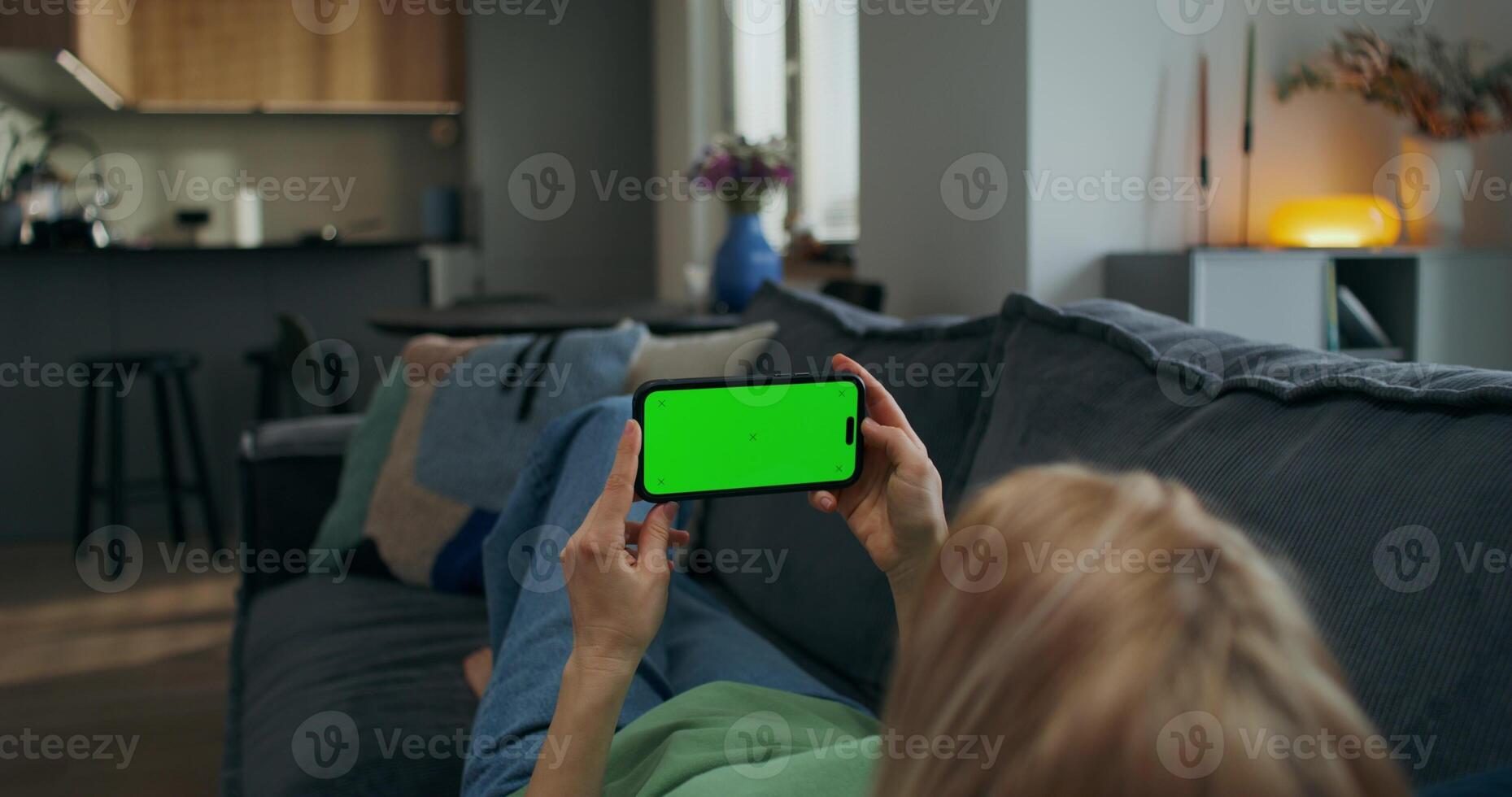 A woman holds a mobile phone with a green screen horizontally in her hands watching , rear view, an unrecognizable person - watching photo
