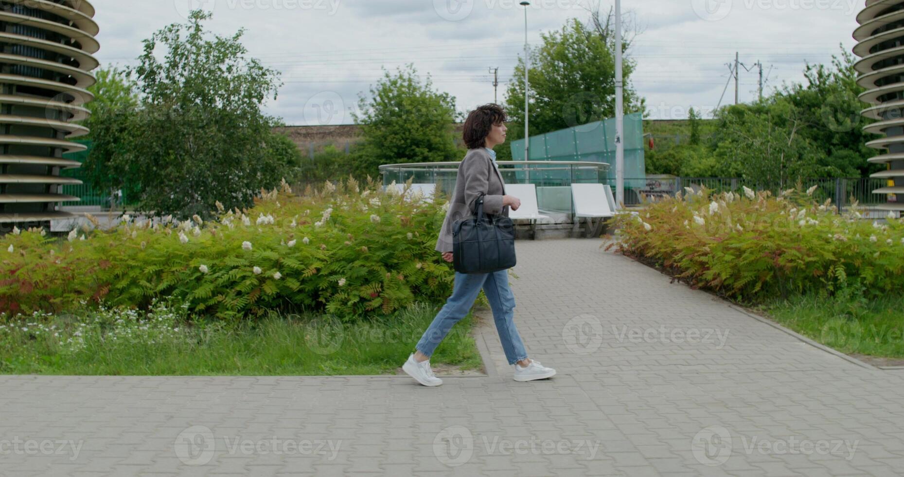 A woman in casual clothes with a bag in her hand walks through the city on a sunny day. Full-length side view photo