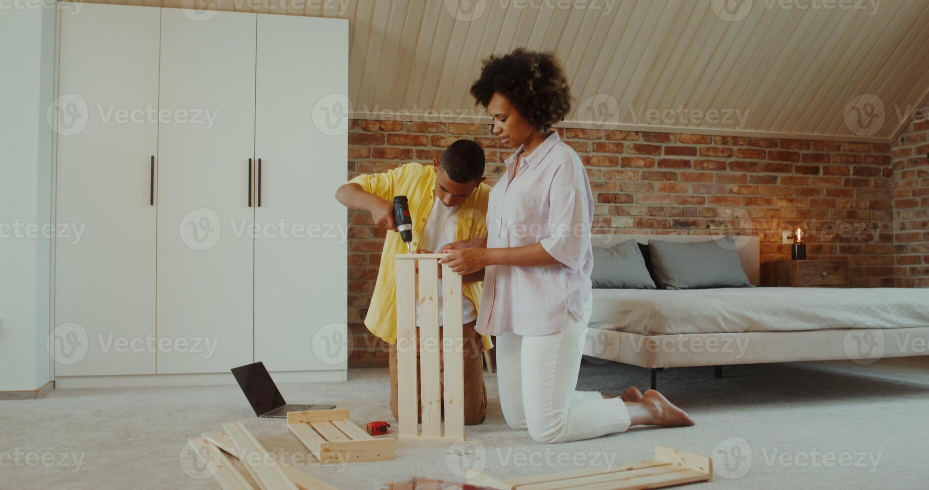 Mom and son make wooden furniture using a drill, sitting on the floor in front of an open laptop at home - sitting photo