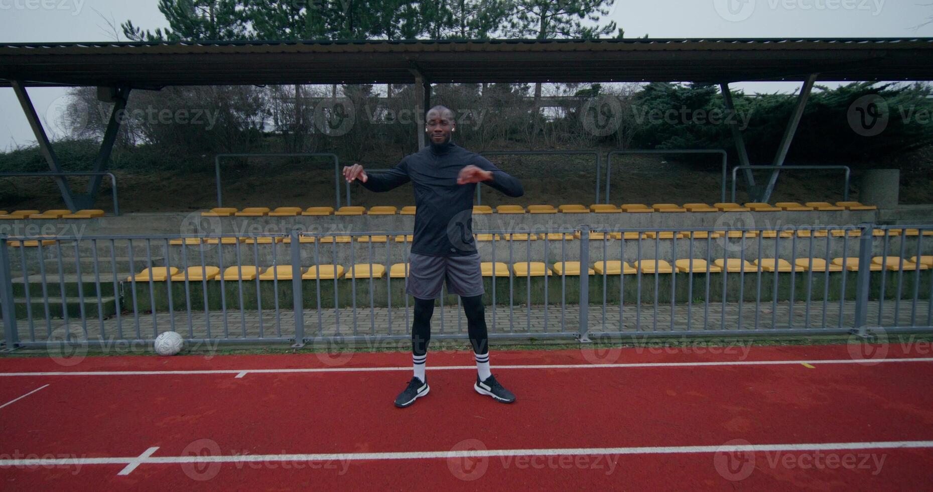 A man in a sports outfit with earphones in his ears does a warm-up standing at the stadium on a cold day - sports photo