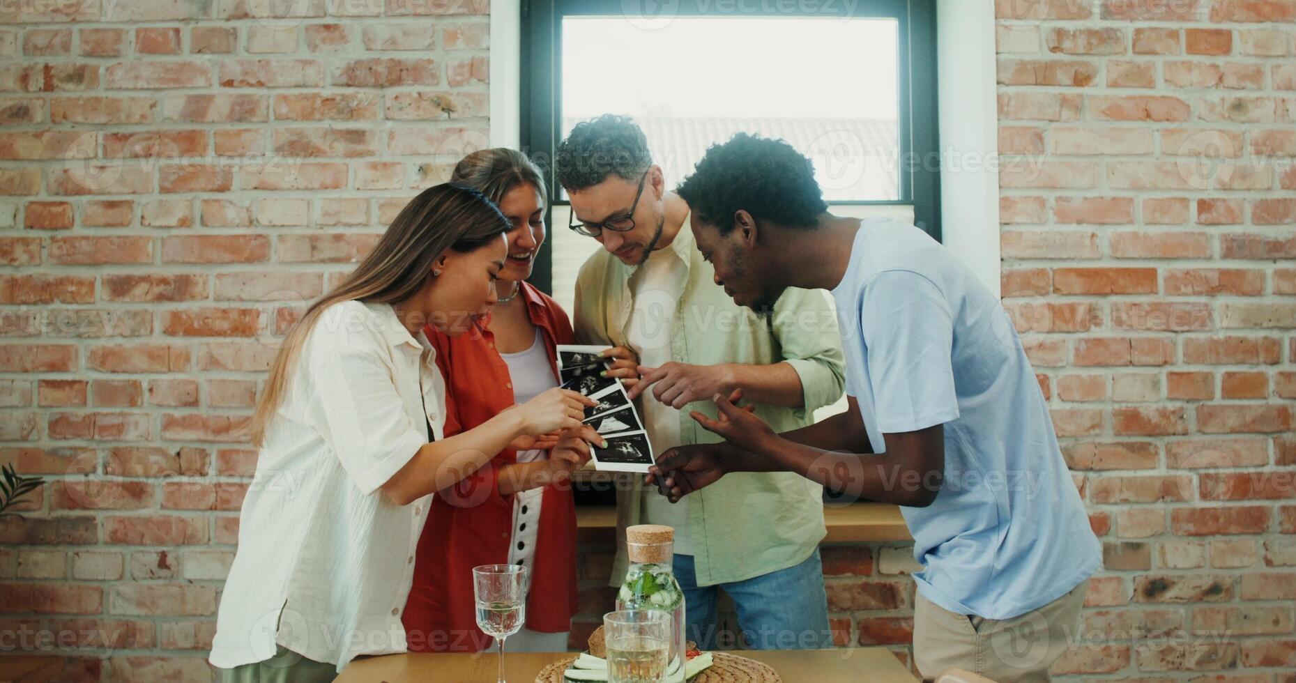 A woman shows her friends ultrasound images sharing the news about her pregnancy, over dinner at home photo