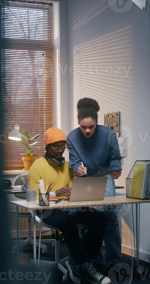 A man and a woman in informal clothes use a laptop and tablet working together in the office photo