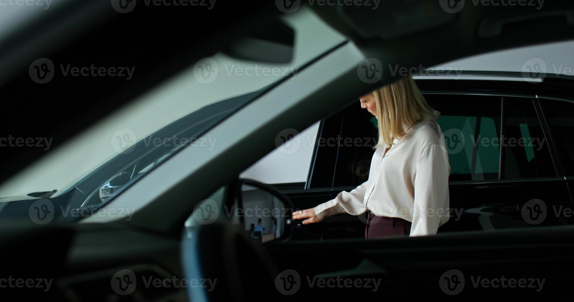 A stylish woman chooses a car by walking around the showroom of a car dealership with a thoughtful look and looking into cars - walking photo