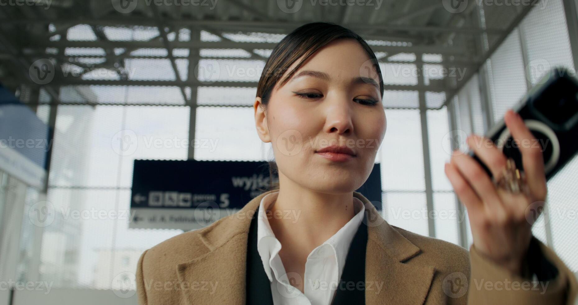 A woman in formal clothes records a voice message on a mobile phone walking through a railway station photo