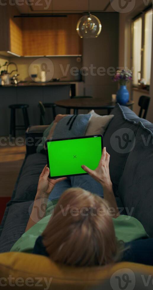 A woman uses a tablet with green screen lying on the couch at home, an unrecognizable person - screen photo