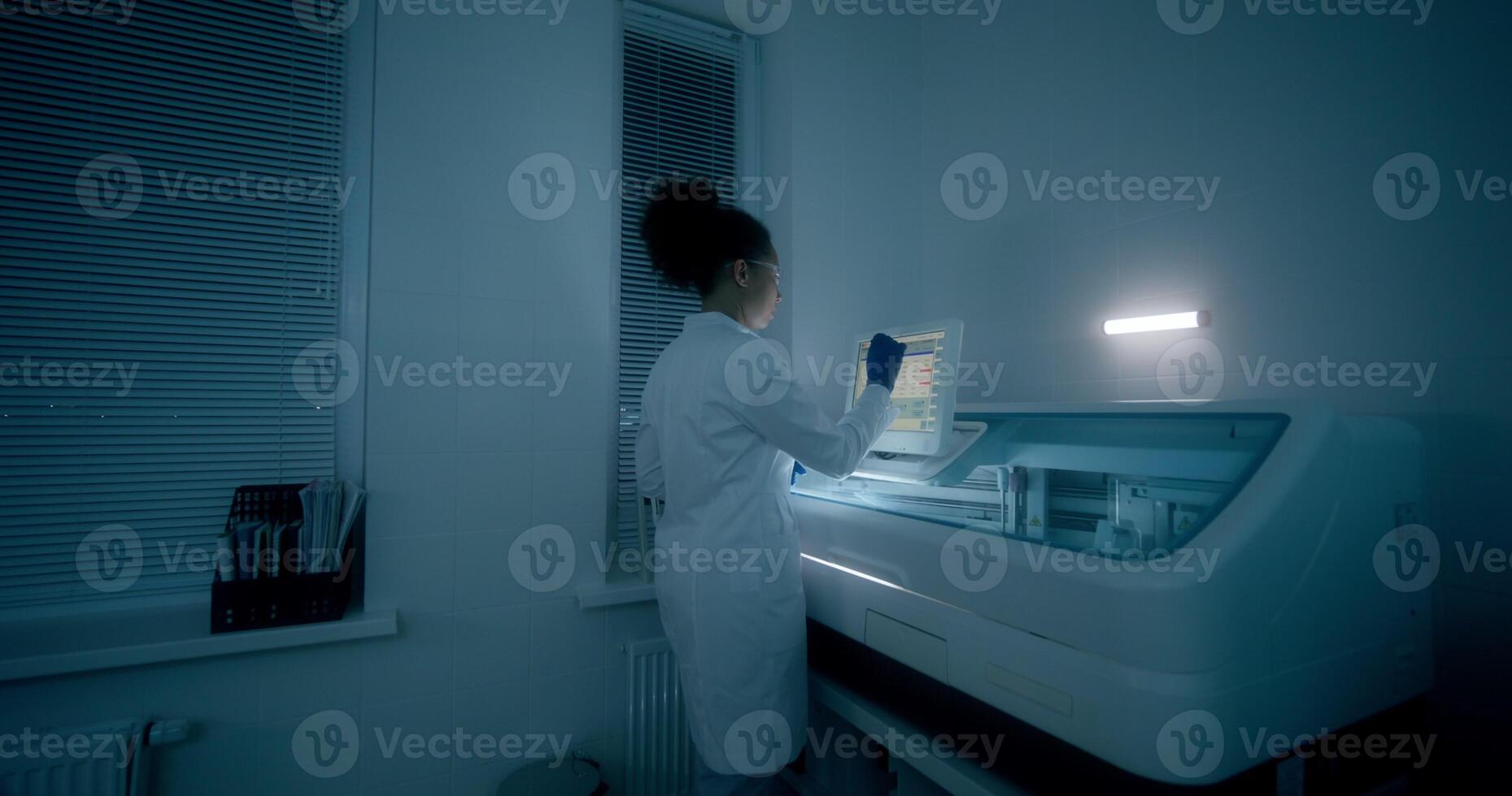 Work in a medical laboratory. A woman in a lab coat, disposable gloves and safety glasses sets up a blood splitting device using a screen photo